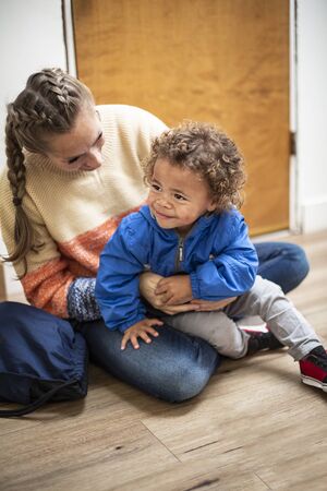 Young bi-racial child being watched by a babysitter. Child care photo of a child care worker sitting with the young boy and smiling togetherの写真素材