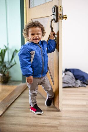 Cute little boy opening the front door to his home. Peeking around with a big smile on his face. Playful fun photo of a 2 year old boyの写真素材