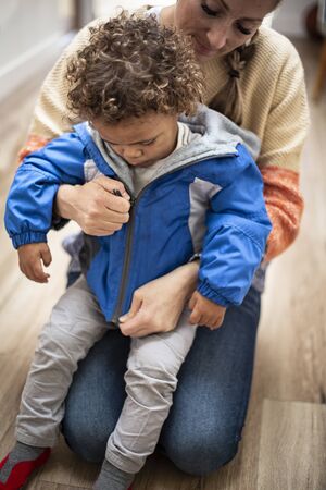 Child care worker putting a jacket on a cute, young bi-racial child. Real candid photo of people Caring for and teaching childrenの写真素材