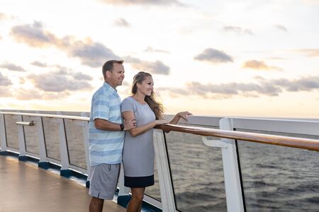 Middle aged couple enjoying a Caribbean Cruise vacation together. Candid photo of a couple enjoying their time on board a cruise ship together. Walking along the deck at sunset and laughing togetherの写真素材
