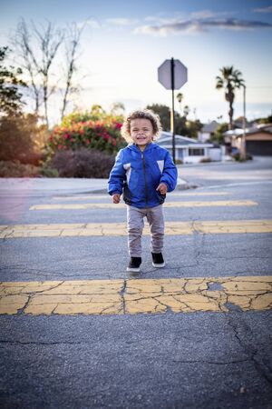 Cute, young bi-racial child walking across the street at the crosswalk. Safety first photo of boy going to preschool early in the morning.の写真素材