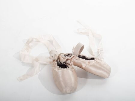 Ballet pointe shoes isolated on white background. Close up view of the shoes of a ballerina sitting on a white floorの写真素材