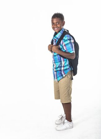 Smiling African American school boy on white background. Wearing a backpack and a plaid shirt and ready to go to school. side viewの写真素材