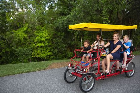 Young happy family riding a double surrey tandem bicycle together. Outdoor summer fun with kidsの写真素材