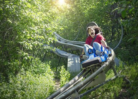 Screaming teen girl riding downhill on an outdoor roller coaster on a warm summer day. She has a fun expression on her face as she enjoys a thrilling ride on an amusement park rideの写真素材