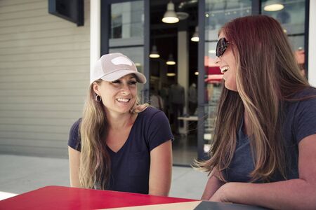 Two women talking and smiling together as they sit at an outdoor cafe in a retail mall. Girlfriends having fun together shopping and eating	 Category	 Lifestyleの写真素材
