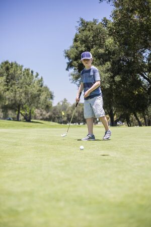 A young boy putting a golf ball on the green while playing golf. Vertical photo of a child learning the game of golfの写真素材