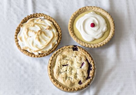 Assorted delicious whole Pies sitting on a table. A view of three different homemade pies - Lemon Meringue, cream and berry pies.の写真素材