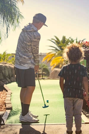 Rear view photo of two boys playing mini golf while on a fun family vacation together.の写真素材