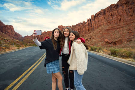 Three teen girls taking a selfie photo together outdoors with beautiful scenic red cliffs in the background.の写真素材