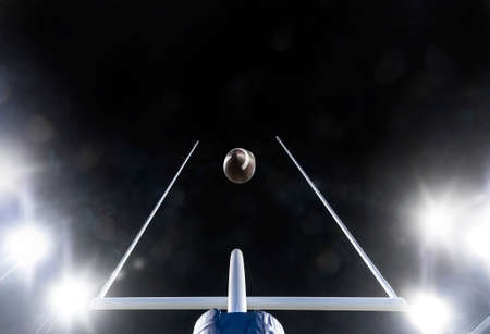 Football flying through the uprights of the field goal posts during a night football gameの写真素材