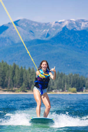 Happy teen girl wake boarding at a picturesque mountain lake on her summer vacation. Boating lifestyleの写真素材