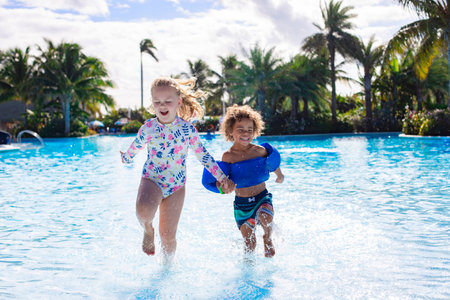 A Cute diverse boy and little girl running and splashing together holding hands in the large...