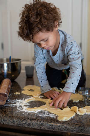 Cute young diverse boy helping in the kitchen making sugar cookies during the Christmas season. Children in the kitchen helping make treatsの写真素材