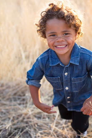 Action photo of a Smiling and active little African American little boy. He runs and plays in an outdoor field with a huge smile on his cute faceの写真素材