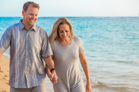 Middle aged couple walking together holding hands on the beach. Sharing a loving moment together while on a beach vacation. Celebrating their anniversaryの写真素材