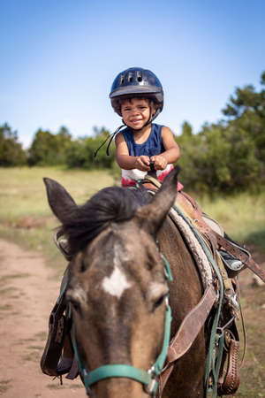 Cute, Smiling little boy riding on a horse. He is happy and enjoying his first pony ride at a mountain ranchの写真素材
