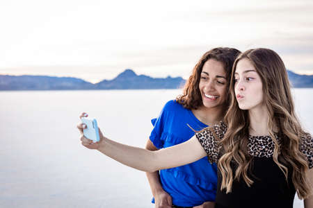Two cute and diverse teenage girls posing and taking a selfie together outdoors on the Bonneville Salt Flatsの写真素材