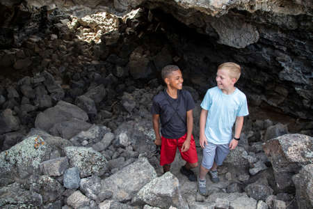 Two diverse boys having fun hiking and exploring in some Lava rock caves. Friends enjoying the great...