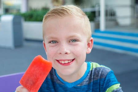 A cute boy eating a strawberry popsicle ice cream treat on a summer day. A Cool treat in the summertime always brings a smileの写真素材