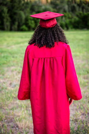 Rear view Portrait of a beautiful multi-ethnic woman wearing her graduation cap and gown. Vertical abstract photo of a diverse college or high school graduateの写真素材