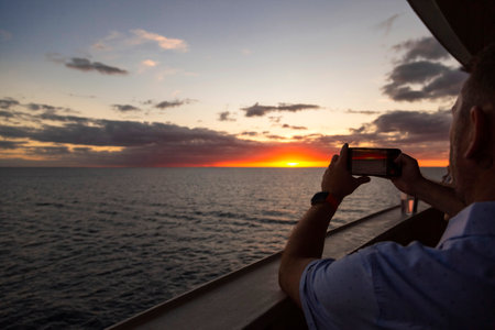 Man taking a photo of the sunset on a cruise ship with a smartphone