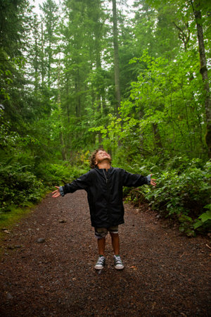 Young African American boy soaking up the beauty of nature while on a walk through a beautiful lush wooded forest in the Pacific Northwest.の写真素材