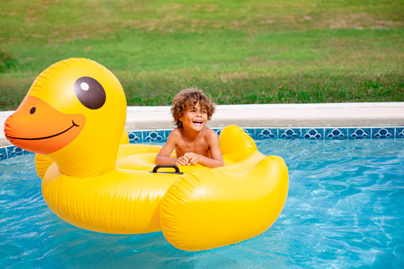 Smiling African American little boy playing in the swimming pool with a large inflatable duck....