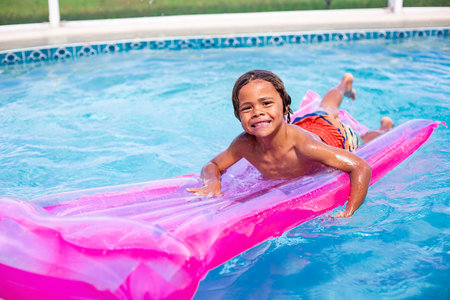 Smiling African American little boy playing in the swimming pool with an inflatable raft. Cute diverse boy having fun in the sun and waterの写真素材