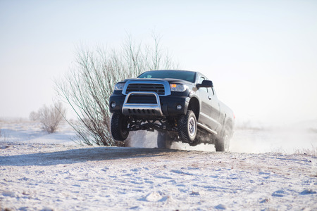 Black truck traveling in the snow and jumping