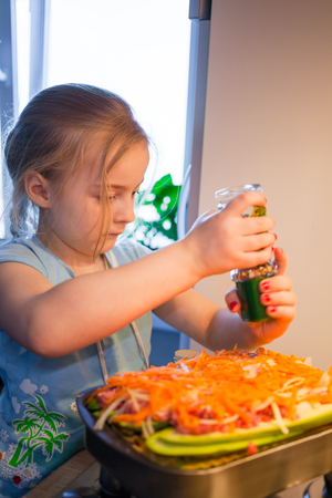 Little girl cooking lasagna, using seasoningの写真素材