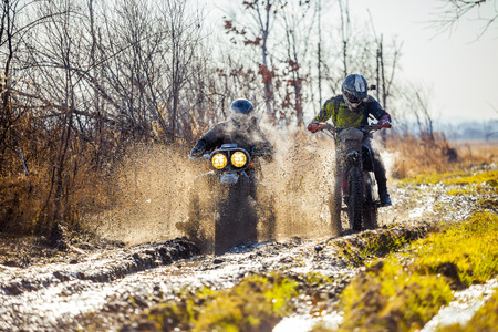 Rally motorbike rider is ahead of another on a dirt road with deep mudの写真素材
