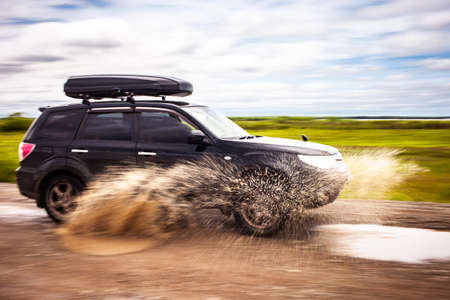 car driving on a  dirt road with puddles. Water splashes from under the wheels. Motion blur