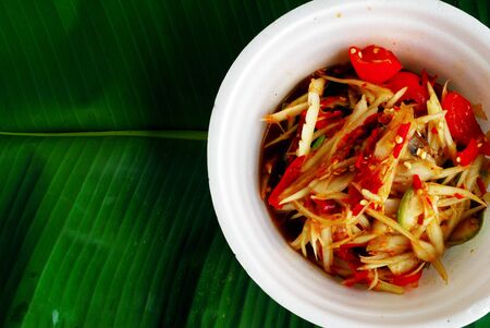 Beautiful colorful papaya salad in a cup made of foam, placed on banana leaves.の写真素材