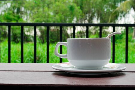Coffee cups, saucers and white coffee spoons on the balcony have a green tree background.の写真素材