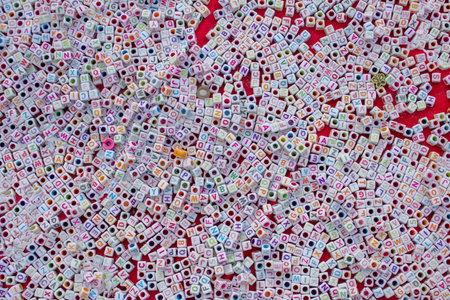 A lot of small white cubes with multi-colored letters and holes lie on a red cloth background....