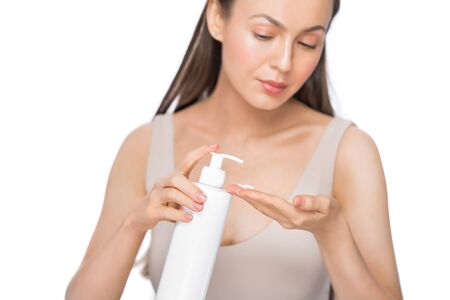 Beauty portrait of an attractive smiling young woman standing isolated over white background, applying body lotion.の写真素材