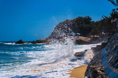 A large wave breaks on the rocks on the beach. White with splashes of sea foam flew high. A wave rolls on the sandy strip of Lamai beach, Koh Samui, Thailand.の写真素材