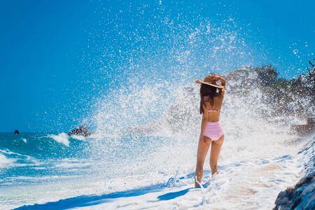 Beautiful girl on a sandy beach against the background of a breaking wave. Sea water splashes up. A...