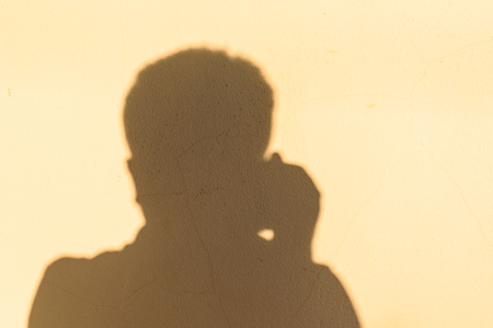 dark shadow man in the house wall, brown wall background, and show hand holding camera