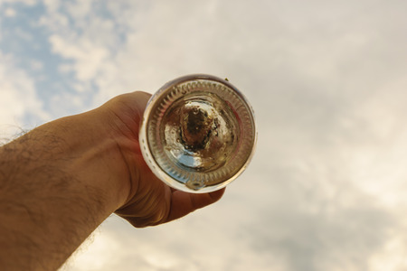Close up to hand holding under of glass bottle,dirty road blurring background, and blue sky blurring backgroundの写真素材