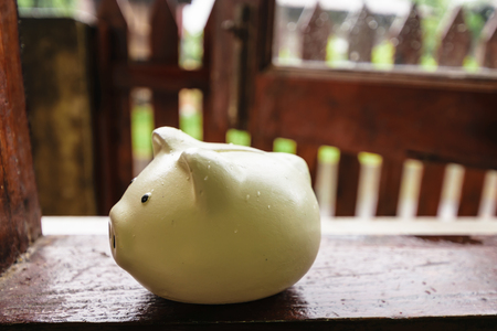 a container for saving money in, especially one shaped like a pig, with a slit in the top through which coins are rich,piggy bank on wooden window in homeの写真素材