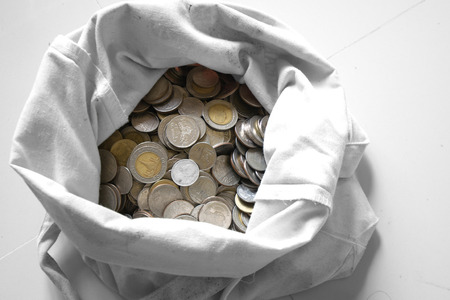 There are silver coins gold coins in an old white bag.white backgroundの写真素材