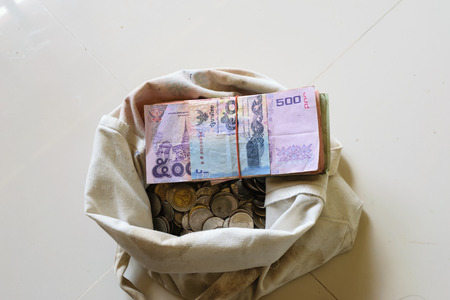 There are silver coins, gold coins and banknote in an old white bag.white backgroundの写真素材