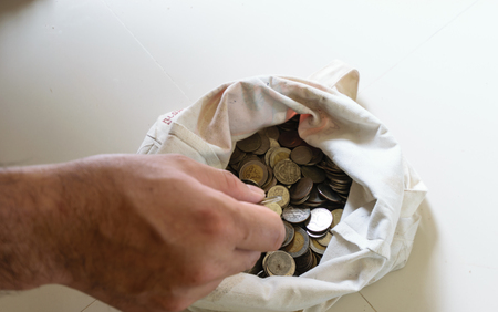The hands are picked up silver coins into the old bag white,with white background ,image focus on a coin cellsの写真素材