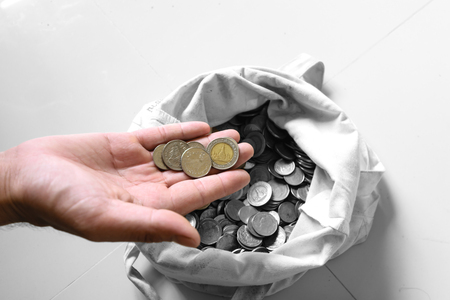 The hands are picked up silver coins into the old bag white,with white background ,image focus on a coin cellsの写真素材