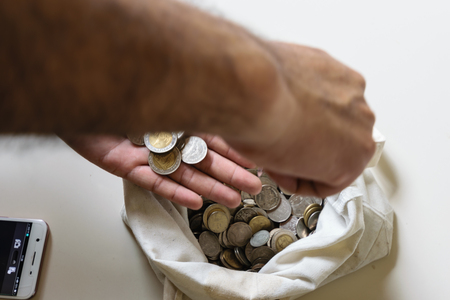 The hands are picked up silver coins into the old bag white,with white background ,image focus on a...