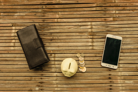 The white pig piggy bank with the money and the phone placed on bamboo table old. Represents a storage saving and creating networks to do business.の写真素材
