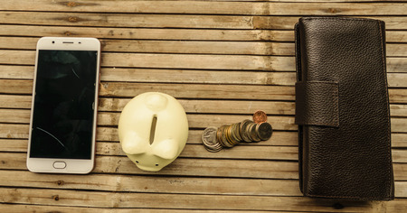 The white pig piggy bank with the money and the phone placed on bamboo table old. Represents a...