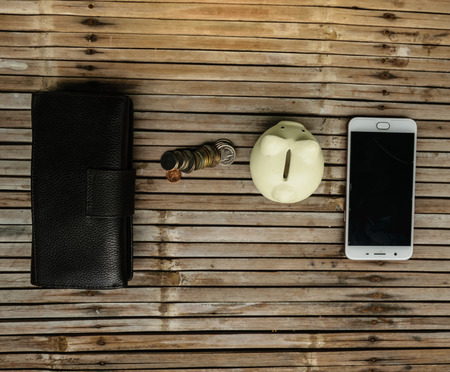 The white pig piggy bank with the money and the phone placed on bamboo table old. Represents a...
